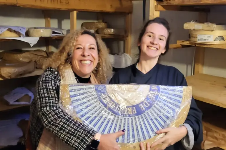Prof. Elaine and a student holding a wheel of Comté cheese in the cellar of a Paris cheese shop